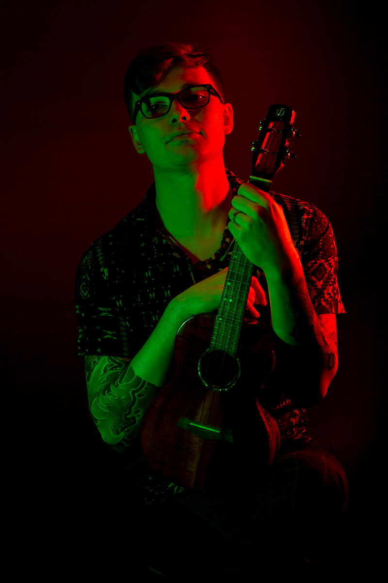 A strikingly lit green and red portrait of Simon with his ukelele